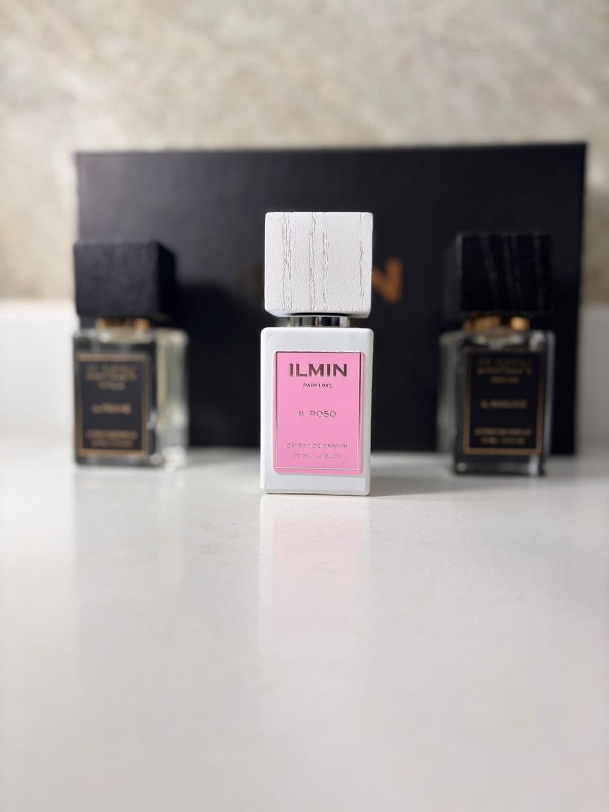 Formato extrait de parfum del catálogo premium Kikluxe Colombia 2026: trío ILMIN Parfums 30ml con IL ROSO blanco y rosa al frente, dos frascos negros y caja negra con dorado — la concentración de alta perfumería que comparte categoría con el Ombre Nomade extrait, envíos 24-48h sin mínimo