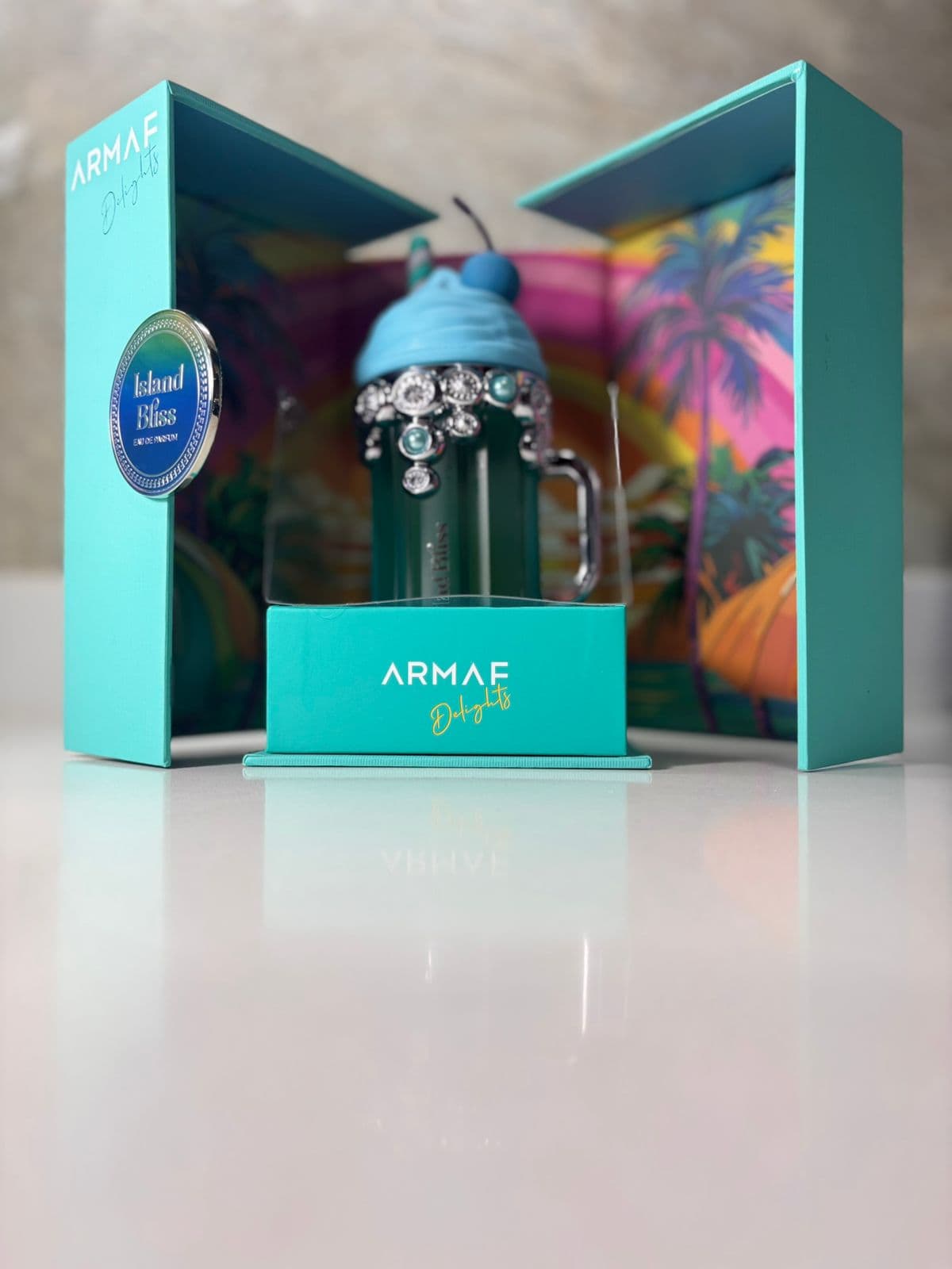 Estuche turquesa desplegable del perfume Armaf Delights Island Bliss EDP con frasco enjoyado en exhibición — ejemplo del empaque premium con que la bodega Kikluxe de Cali despacha perfumes importados, el mismo cuidado de embalaje doble burbuja que protege cada frasco Valentino Born in Roma enviado a las 13 ciudades de Colombia