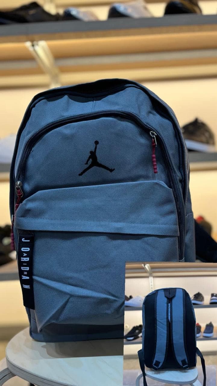 Morral Jordan gris con jumpman negro al por mayor Colombia 2026: doble compartimento con bolsillo laptop y zipper pull rojo desde $70.000 COP — Kikluxe bodega mayorista de morrales importados Triple AAA, envío desde 1 unidad a toda Colombia