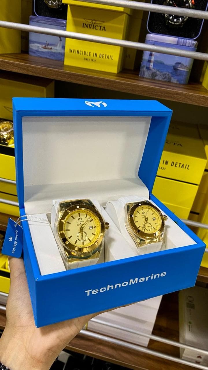 Set pareja de relojes TechnoMarine Cruise dorados con correa de silicona blanca en caja original azul, junto a cajas Invicta en la bodega — relojes de marca al por mayor Colombia 2026 desde $150.000 COP el set, Kikluxe envíos 24-48h sin mínimo